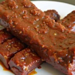 Juicy and tender beef ribs coated in a rich barbecue sauce on a white plate with a fork.