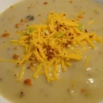 Hamburger Potato Soup topped with shredded cheddar cheese and green onions in a white bowl.